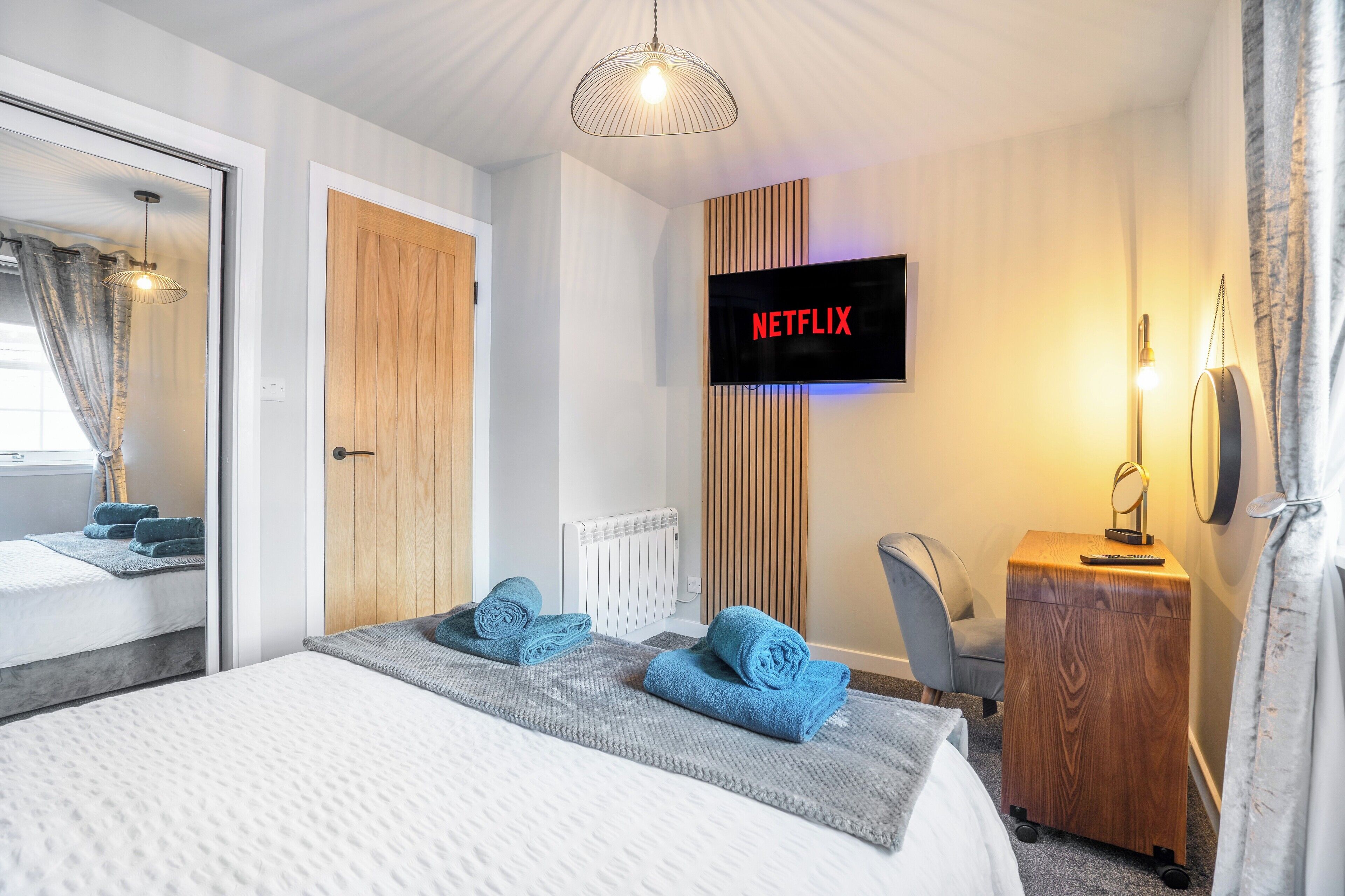 Une chambre d’hôtel comprenant un lit, un téléviseur fixé au mur, une armoire en bois, un bureau avec une lampe et un miroir.