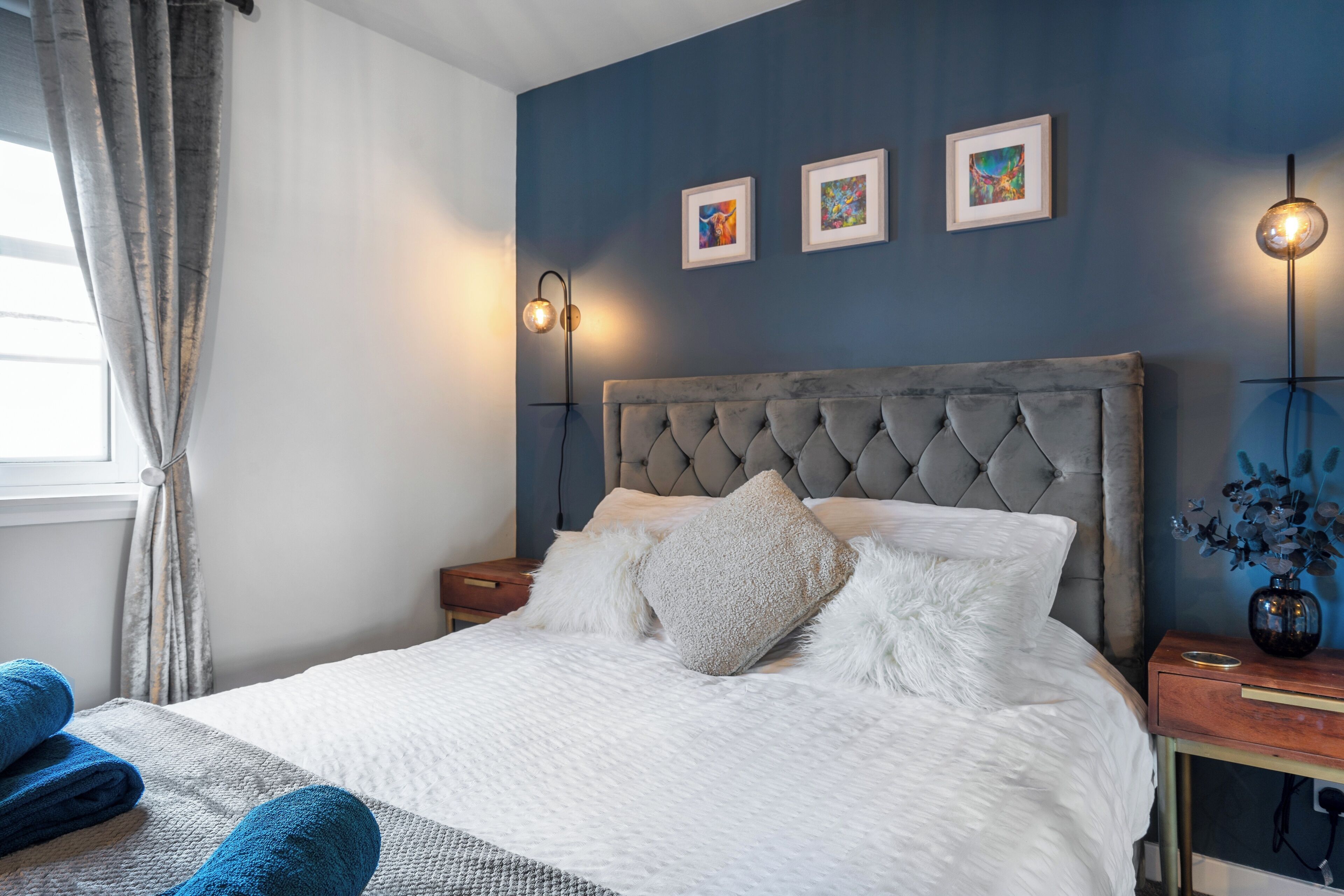 A neatly made bed with a tufted headboard, a bedside table with a lamp, and artwork on the wall.