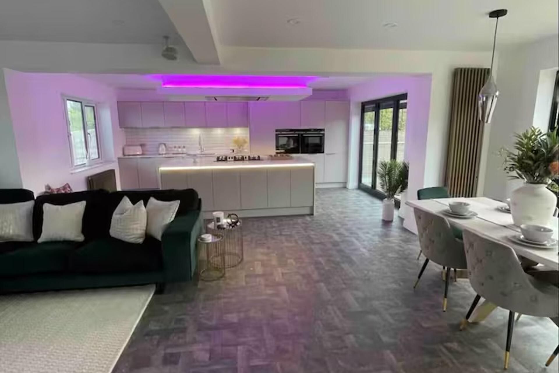Een moderne woonkamer met een groene bank, een eethoek met een tafel en stoelen, en een keuken met een centraal kookeiland.