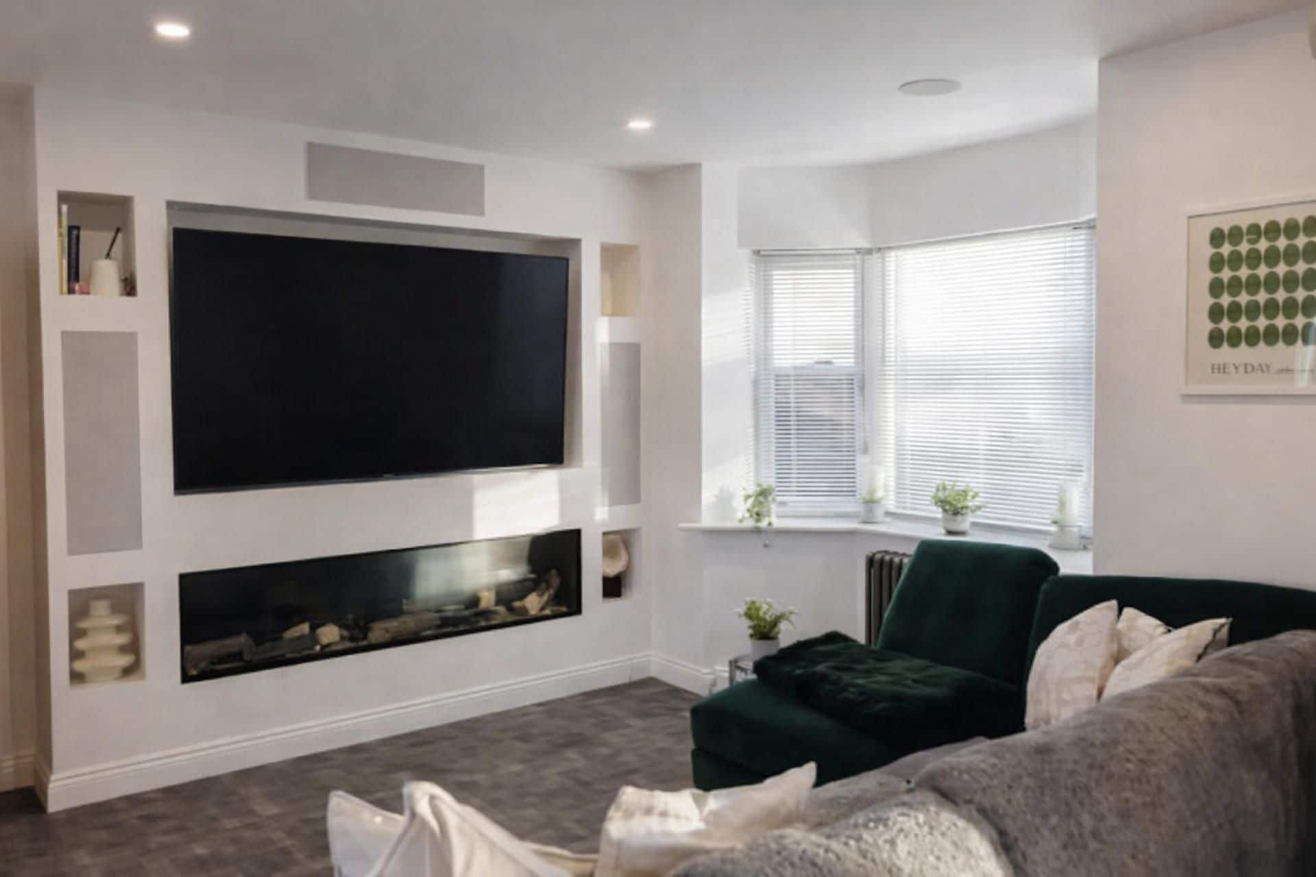 Una sala de estar moderna con un televisor de pantalla plana grande montado en la pared, una chimenea debajo, un sofá verde y una ventana con persianas.