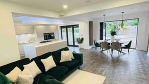 Un salon moderne avec un canapé vert, un coin repas avec une table et des chaises, et une cuisine en arrière-plan.