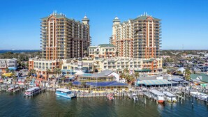 Um hotel na orla marítima com vários edifícios altos, um porto com barcos e um calçadão com lojas.