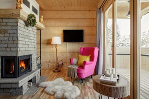 A cozy room with a fireplace, a pink chair, a standing lamp, and a television on the wall.
