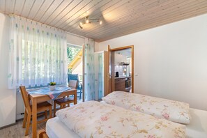 A bedroom with a bed, a table, and a chair. There is a window with curtains and a view of the outside. - Apartment 'Rose' with Private Terrace, Shared Garden and Wi-Fi (Bad Peterstal-Griesbach)