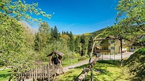 A wooden play structure, a building with a red roof, and a road leading to it. - Apartment 'Rose' with Private Terrace, Shared Garden and Wi-Fi (Bad Peterstal-Griesbach)