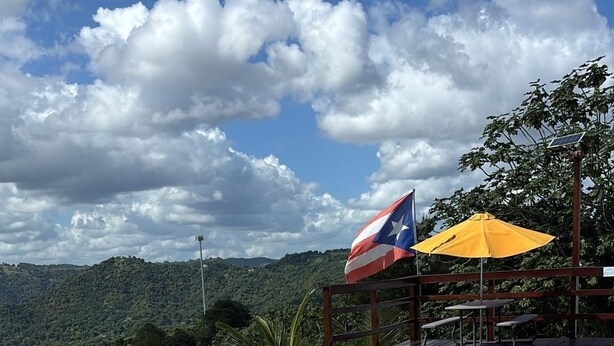 Una piscina con vistas a un paisaje montañoso, una bandera y un paraguas amarillo.
