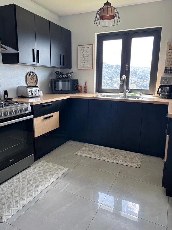A modern kitchen with black cabinets, a stainless steel stove, a microwave, and a large window with a mountain view.