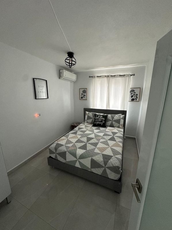 Un dormitorio con una cama, un aire acondicionado instalado en la pared, una cita inspiradora enmarcada y una imagen de flores enmarcada.