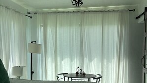 Un dormitorio con una cama, una mesa con una bicicleta, una lámpara y cortinas de tela ligera.