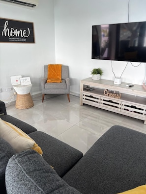 Una sala moderna con un sofá gris, un sillón gris con una manta naranja, un televisor sobre un mueble de madera y un letrero que dice 'home'.
