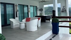 Un patio exterior moderno con mobiliario blanco, una mesa de billar y vistas a las montañas.