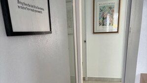 Un pasillo con una cita enmarcada en la pared, una fotografía enmarcada de flores silvestres y una puerta al final.