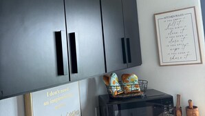 Una cocina con armarios oscuros, microondas, tostadora y una cita inspiradora enmarcada en la pared.