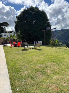 An outdoor seating area with chairs and tables, a large tree, and a view of a mountain range.