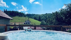 Ein Whirlpool mit Holzterrasse, ein Haus im Hintergrund und ein grüner Hügel.