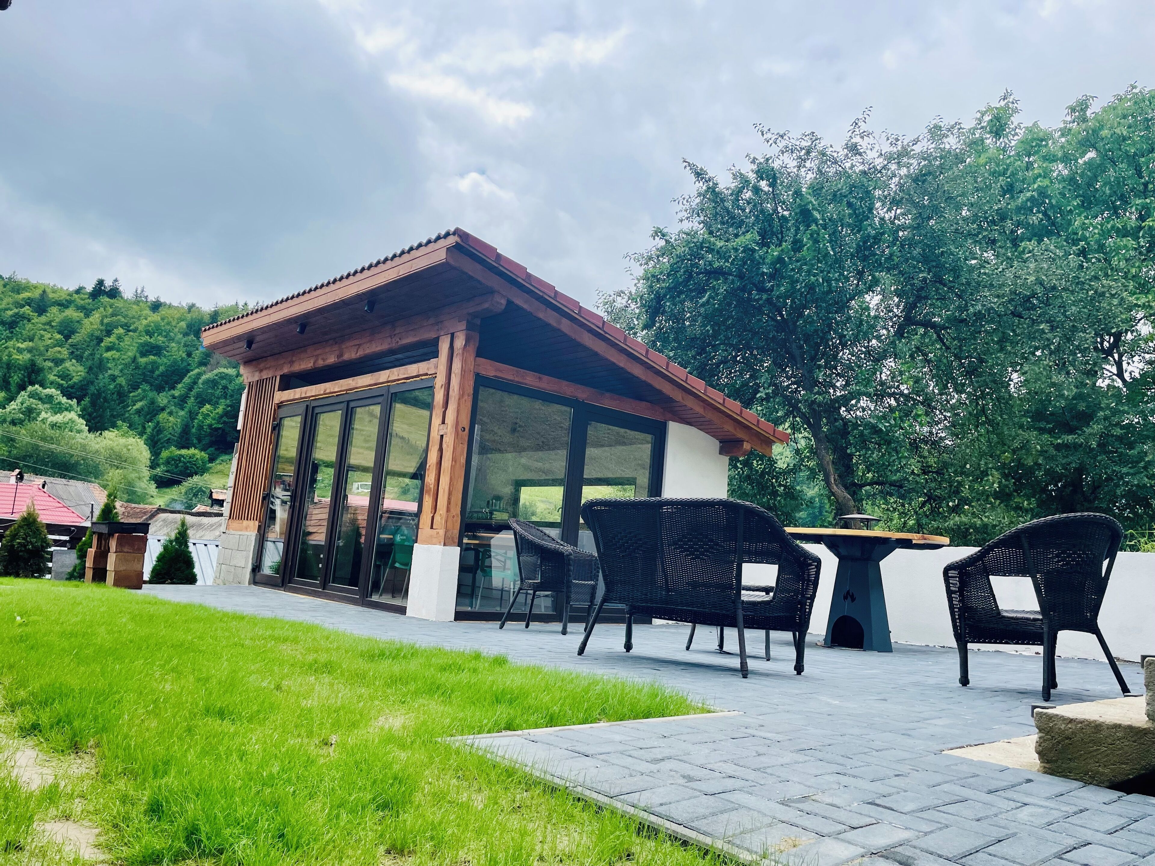 A covered outdoor seating area with a table and chairs, surrounded by a grassy lawn and a paved walkway.