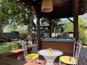 A covered outdoor seating area with a hot tub, two yellow chairs, and a television. - poolside getaway w/hot tub & relaxing courtyard (Houston)