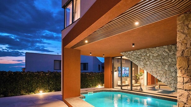 Uma casa moderna com piscina, muro de pedra e interior bem iluminado.