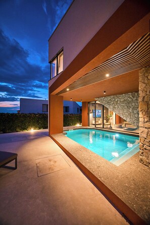 Una casa moderna con piscina, muro de piedra y un interior bien iluminado.