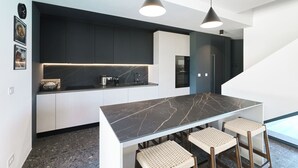 Cozinha moderna com bancada de mármore, dois bancos altos e iluminação pendente.