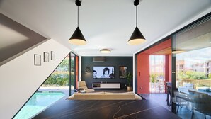 Uma área de jantar moderna com uma grande mesa de mármore preto, duas luzes pendentes, um sofá e uma televisão.