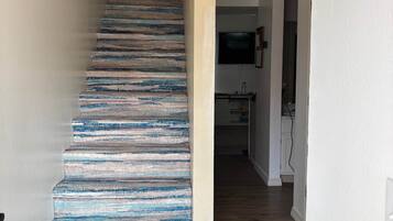 A staircase with a blue and white striped carpet, a white wall with a 'BE' sign, and a kitchen area in the background.