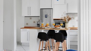 Una cocina moderna con armarios blancos, un refrigerador de acero inoxidable y una encimera de madera. Hay tres sillas negras en la isla y un florero con plantas secas sobre la encimera.