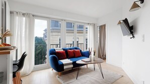 Un salón moderno con un sofá azul, una mesa de centro y vistas de un paisaje urbano a través de amplios ventanales.