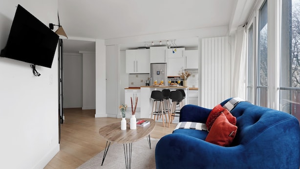 Una sala de estar moderna con un sofá azul, una mesa de centro de madera y un televisor de pantalla plana montado en la pared.