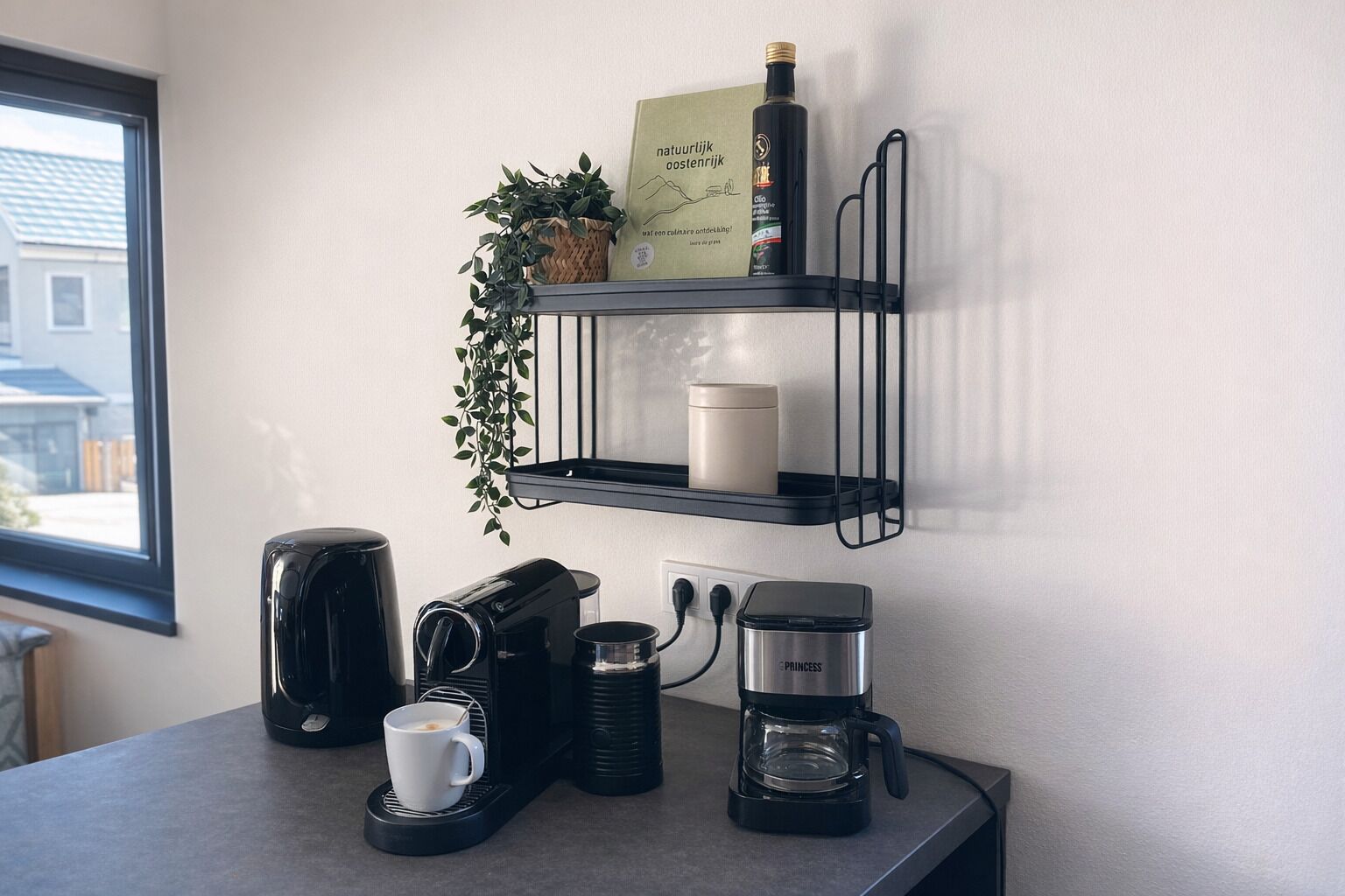 A kitchen counter with coffee makers, a mug, a candle, and a bottle on a black shelf.