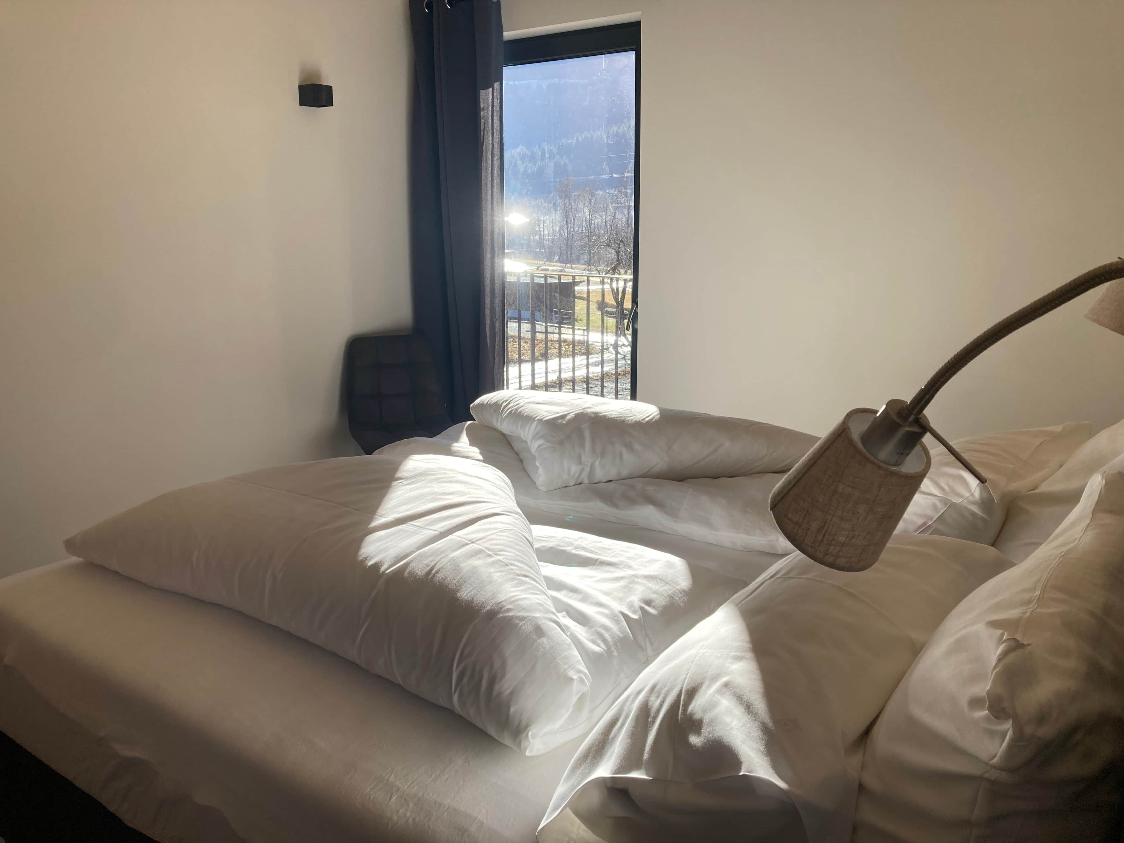 A hotel room with a bed, a chair, a window with a view of a snowy landscape, and a lamp.