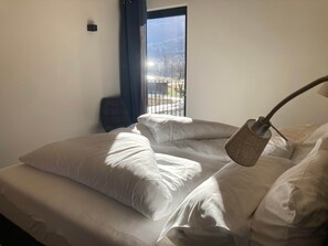 A hotel room with a bed, a chair, a window with a view of a snowy landscape, and a lamp.