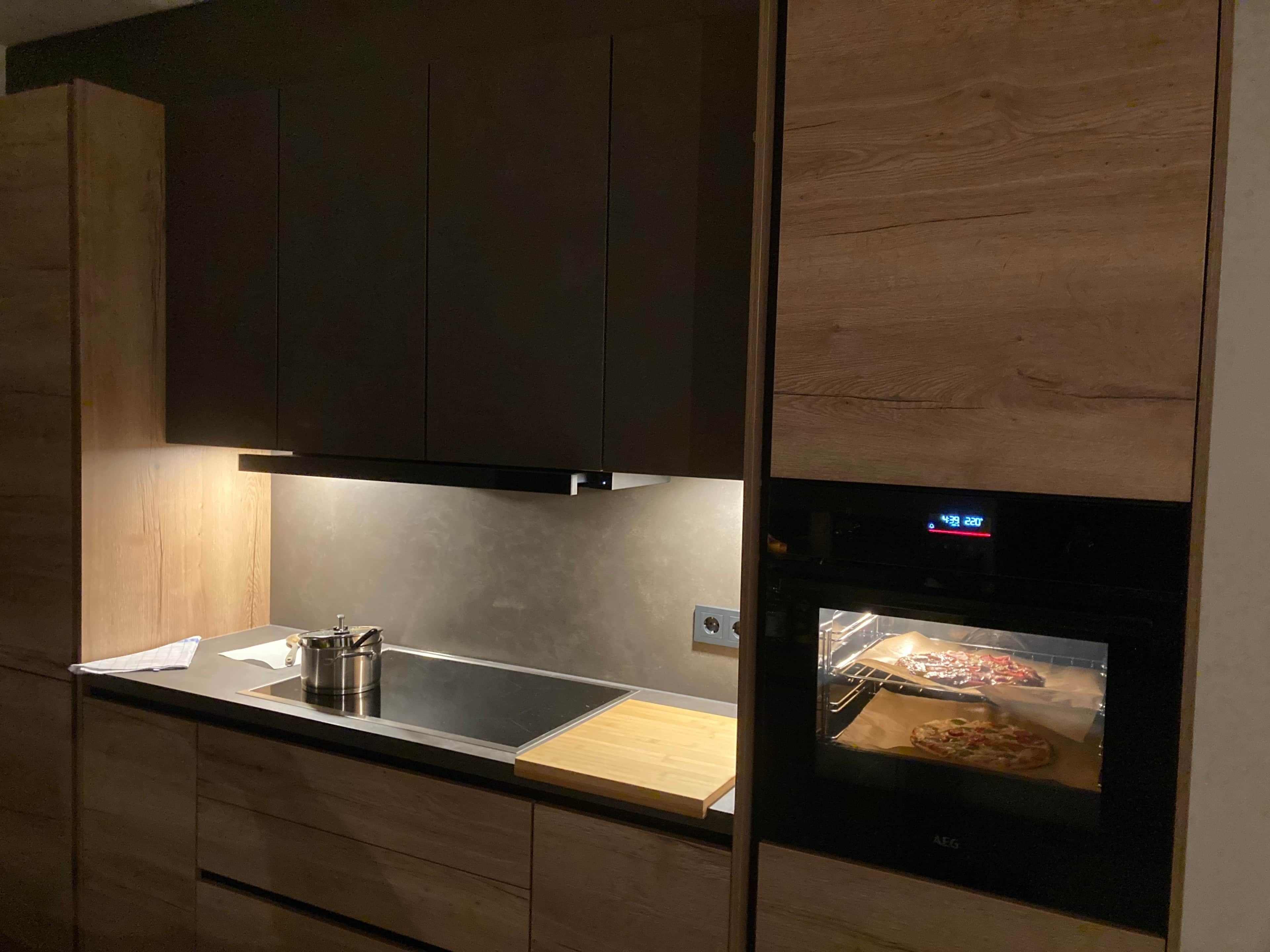 A modern kitchen with dark cabinets, a stainless steel countertop, and a built-in oven.