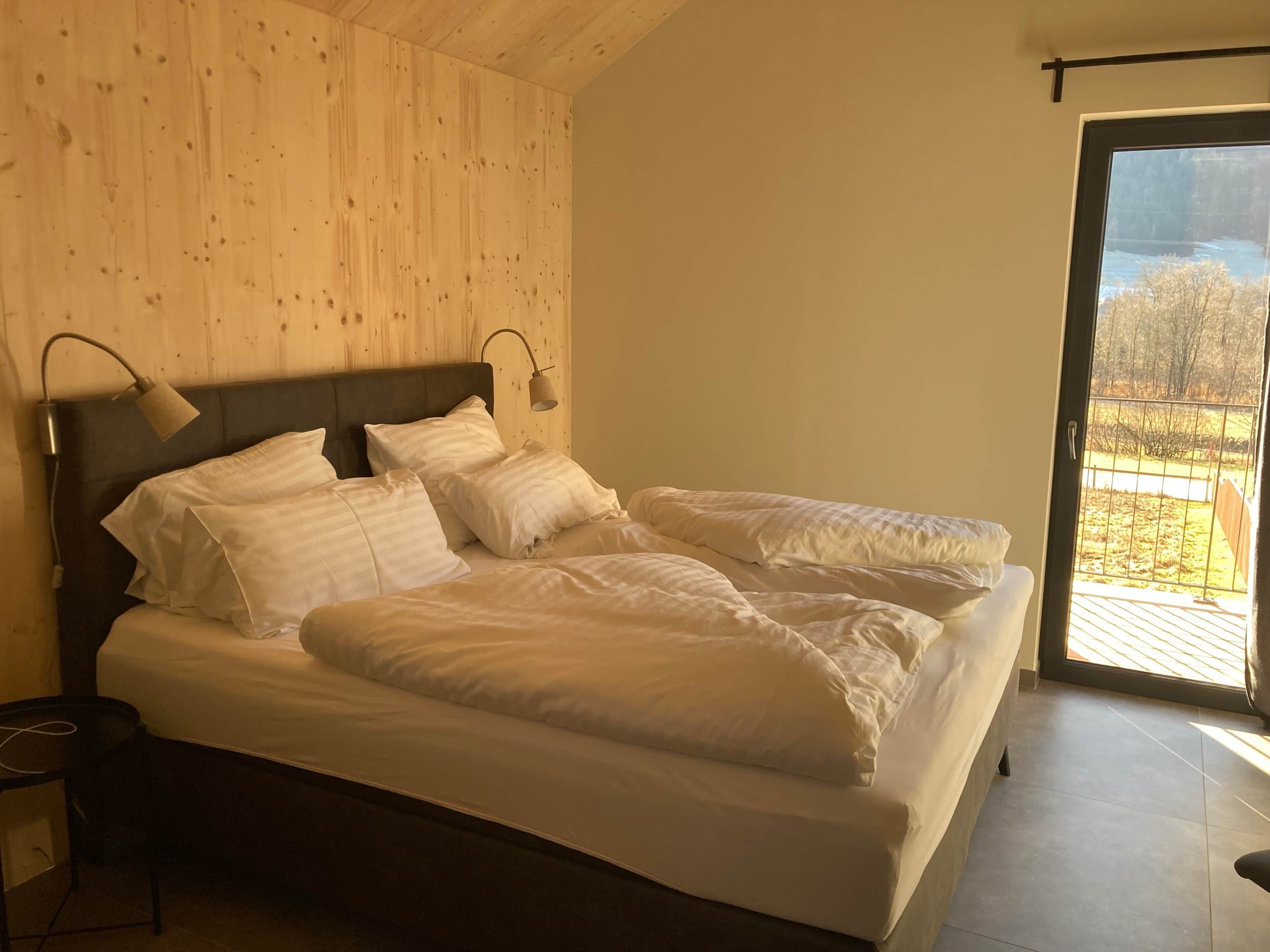 A bedroom with a bed, two bedside lamps, a nightstand, and a view through a glass door.