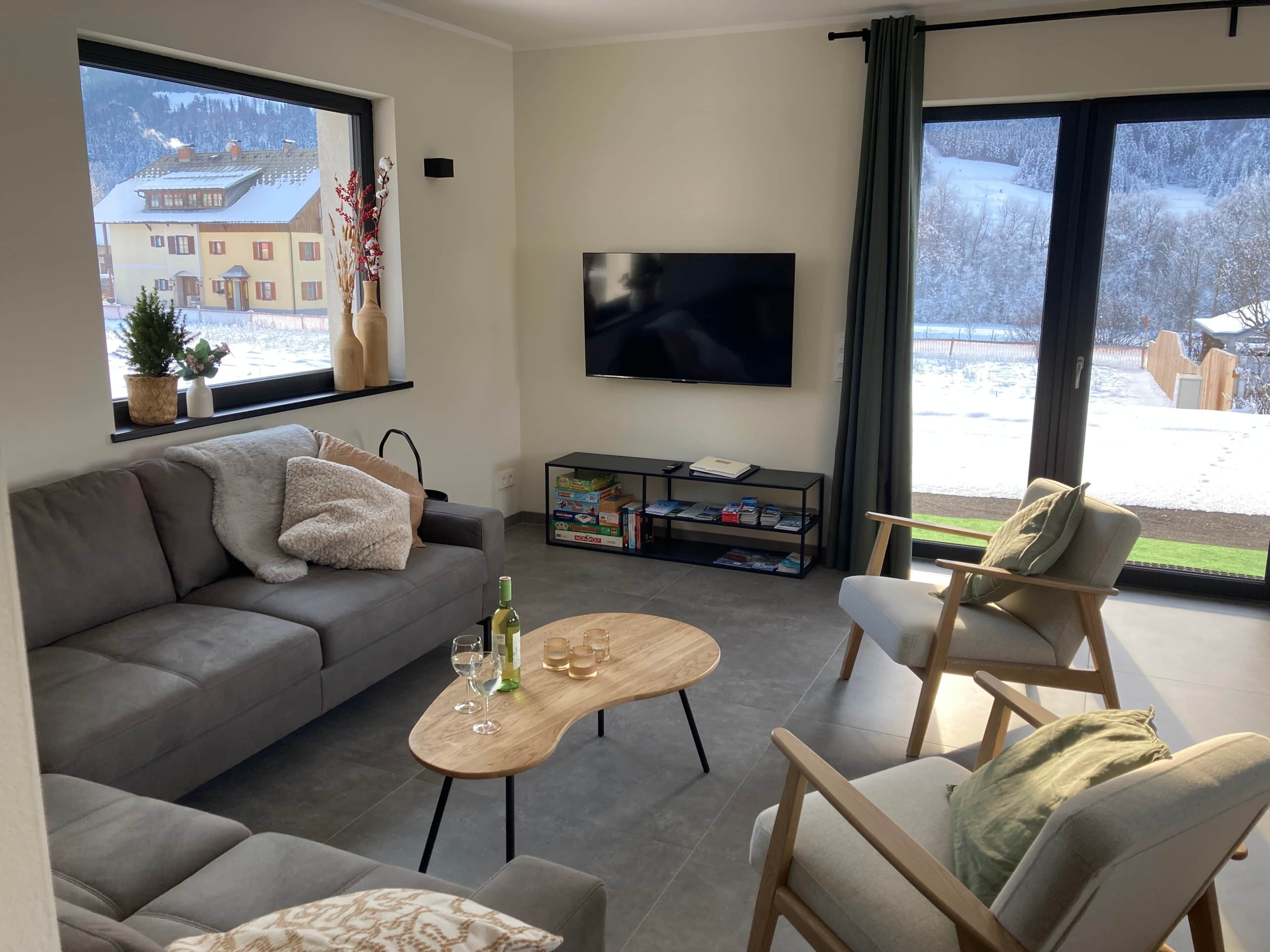 A modern living room with a grey sofa, a wooden coffee table, and a TV on the wall.