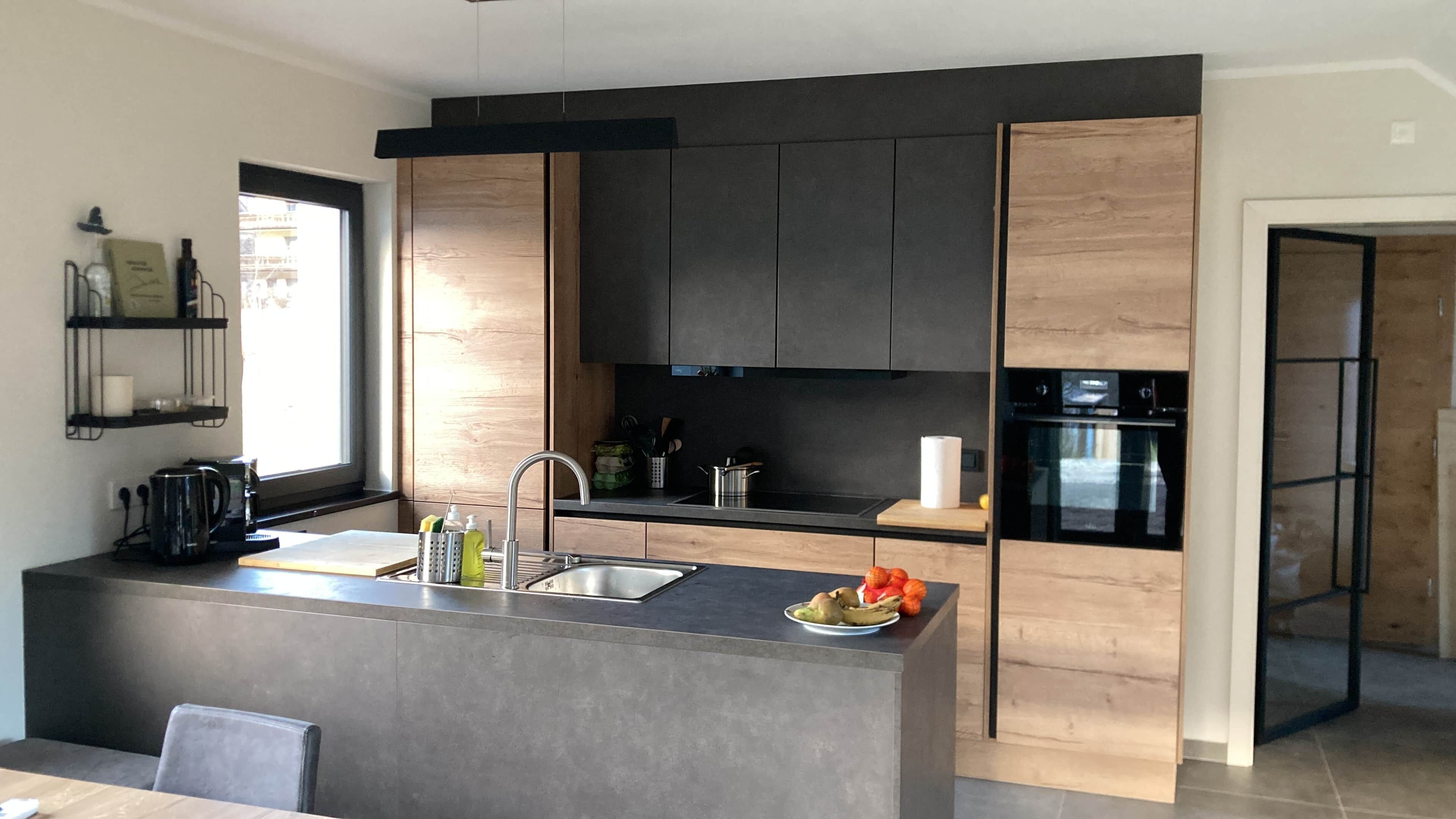 A modern kitchen with a central island, dark cabinetry, and a built-in oven.