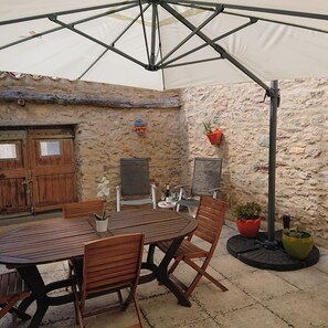 A stone-walled patio with a wooden table and chairs, a hanging plant, and a potted plant.