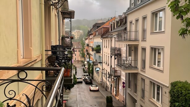 Una calle estrecha con coches estacionados, balcones y edificios de varios pisos.