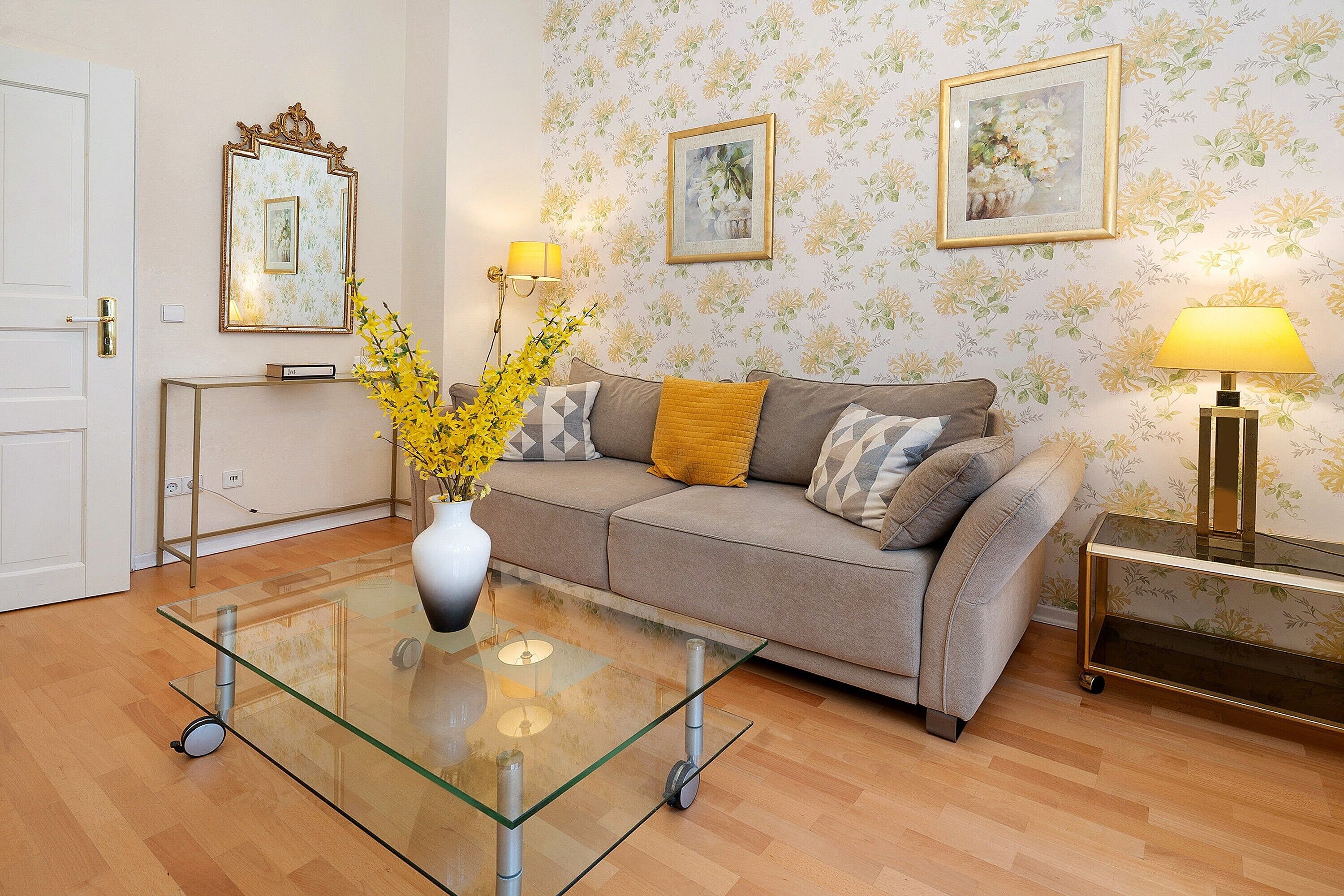 A living room with a glass coffee table, a sofa, a side table, and a lamp.