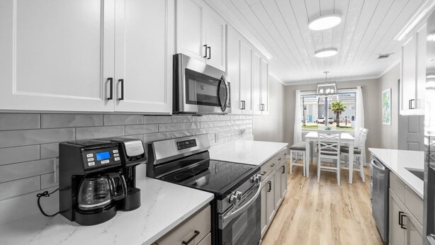 A modern kitchen with white cabinets, a microwave, a coffee maker, and a dining area with a table and chairs. - Beach Bear Townhome: Steps to Sand & Schooners, Pet Friendly, Private Yard (Panama City Beach)
