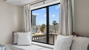 A balcony with a cushioned seating area, a view of a residential area, and a building in the background. - Beach Bear Townhome: Steps to Sand & Schooners, Pet Friendly, Private Yard (Panama City Beach)