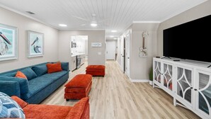 A modern living room with a blue sofa, red ottomans, a TV, and artwork on the walls. - Beach Bear Townhome: Steps to Sand & Schooners, Pet Friendly, Private Yard (Panama City Beach)