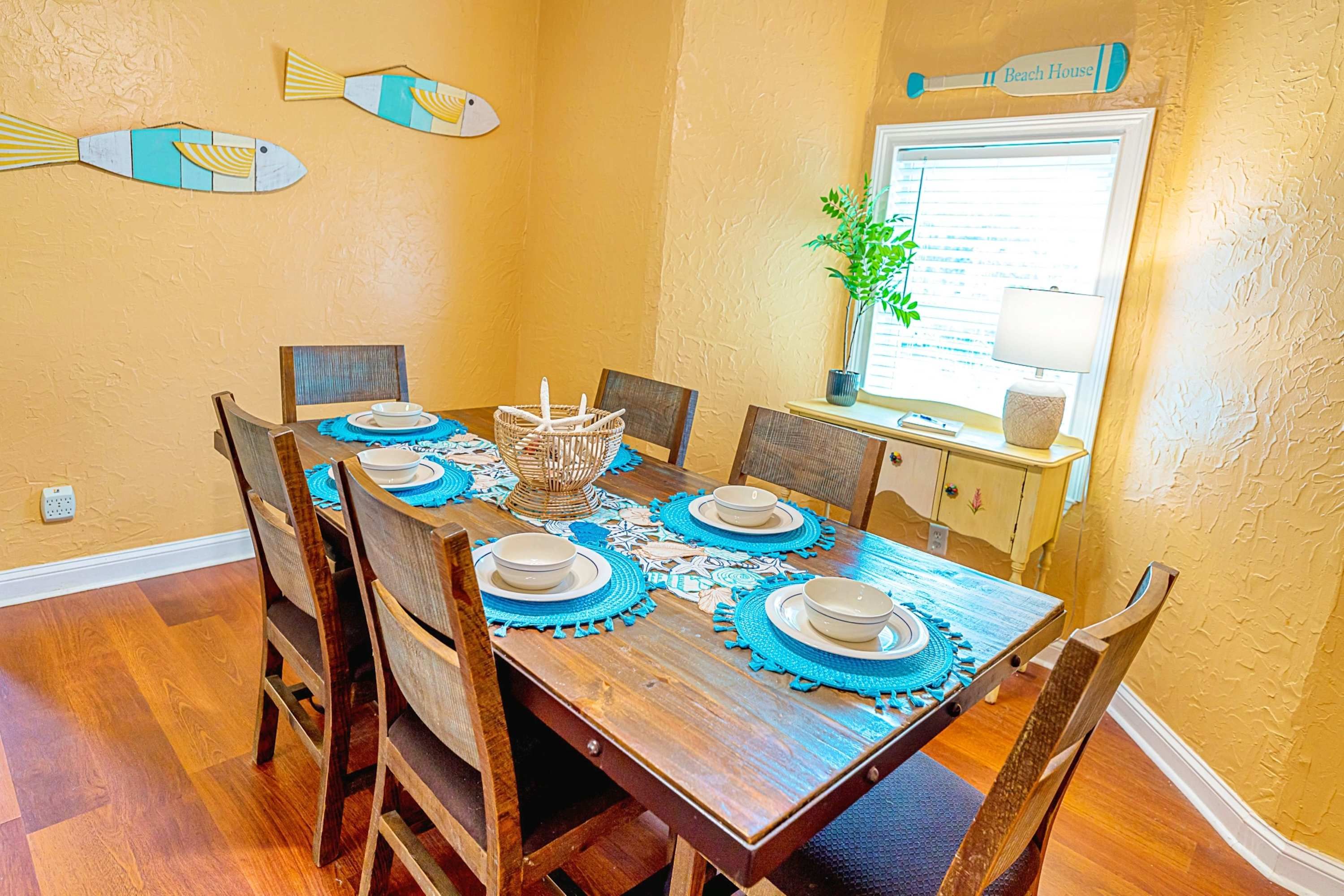 Comedor con mesa de madera dispuesta para cuatro personas, rodeada de seis sillas.