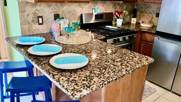 Una cocina con encimeras de granito, armarios de madera, estufa de acero inoxidable y taburetes de bar azules.