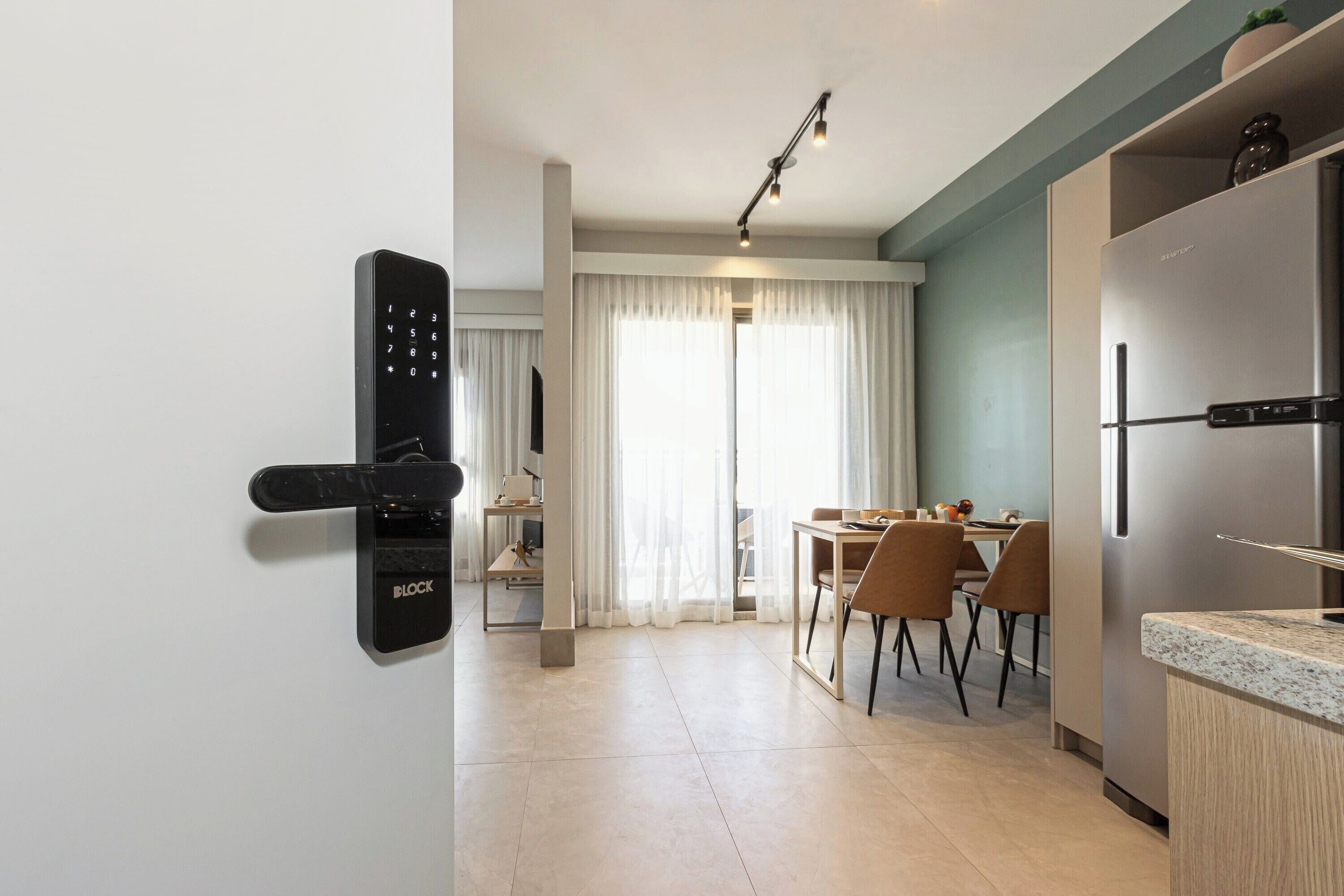 A modern kitchen with a built-in refrigerator, a dining area with a table and chairs, and a wall-mounted electronic lock.