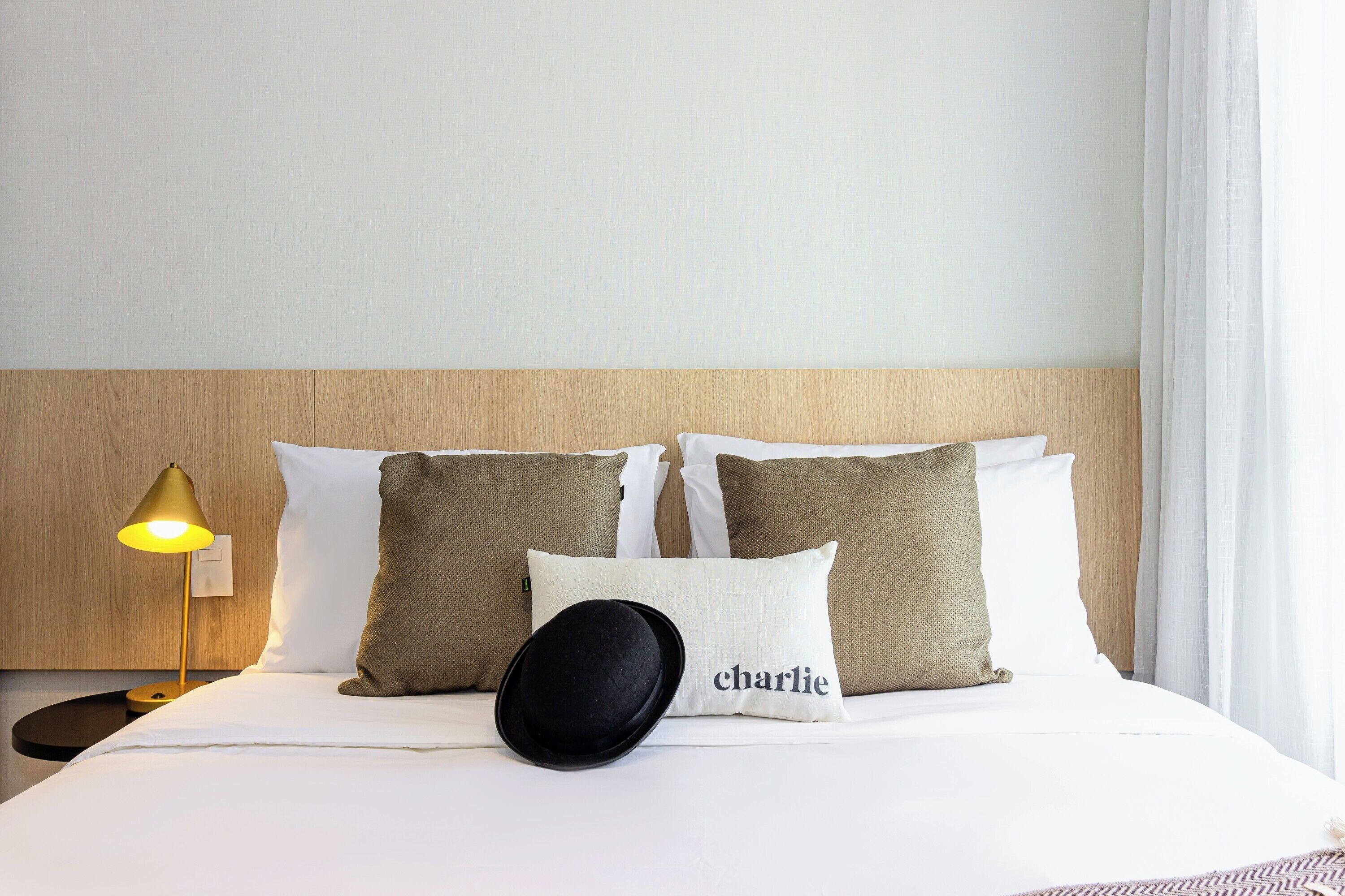Una habitación de hotel con cama, almohadas, una lámpara y una mesita de noche.