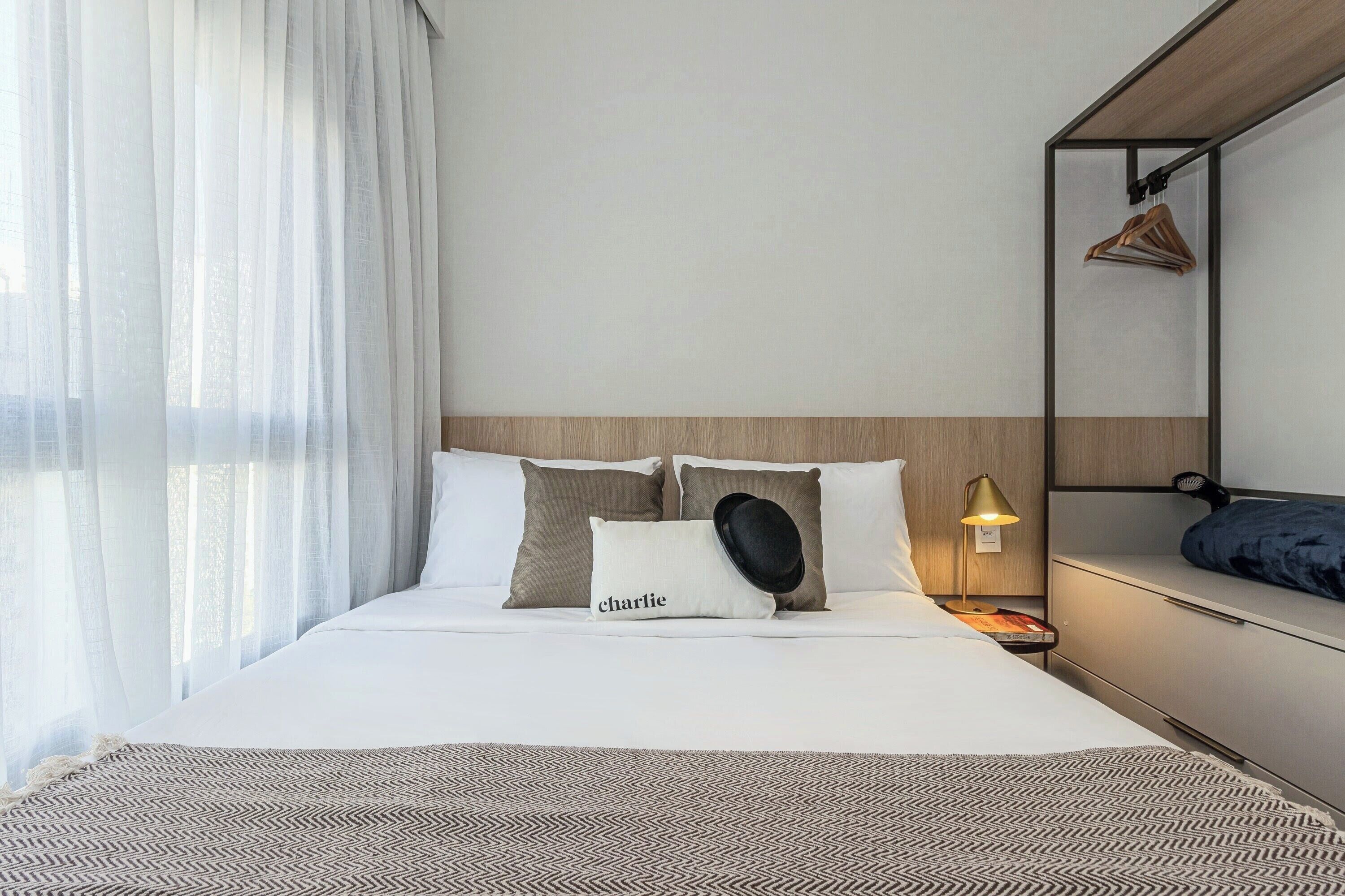 Ein Hotelzimmer mit Bett, Nachttisch mit Lampe, Kleiderhaken und einem an der Wand befestigten Spiegel.