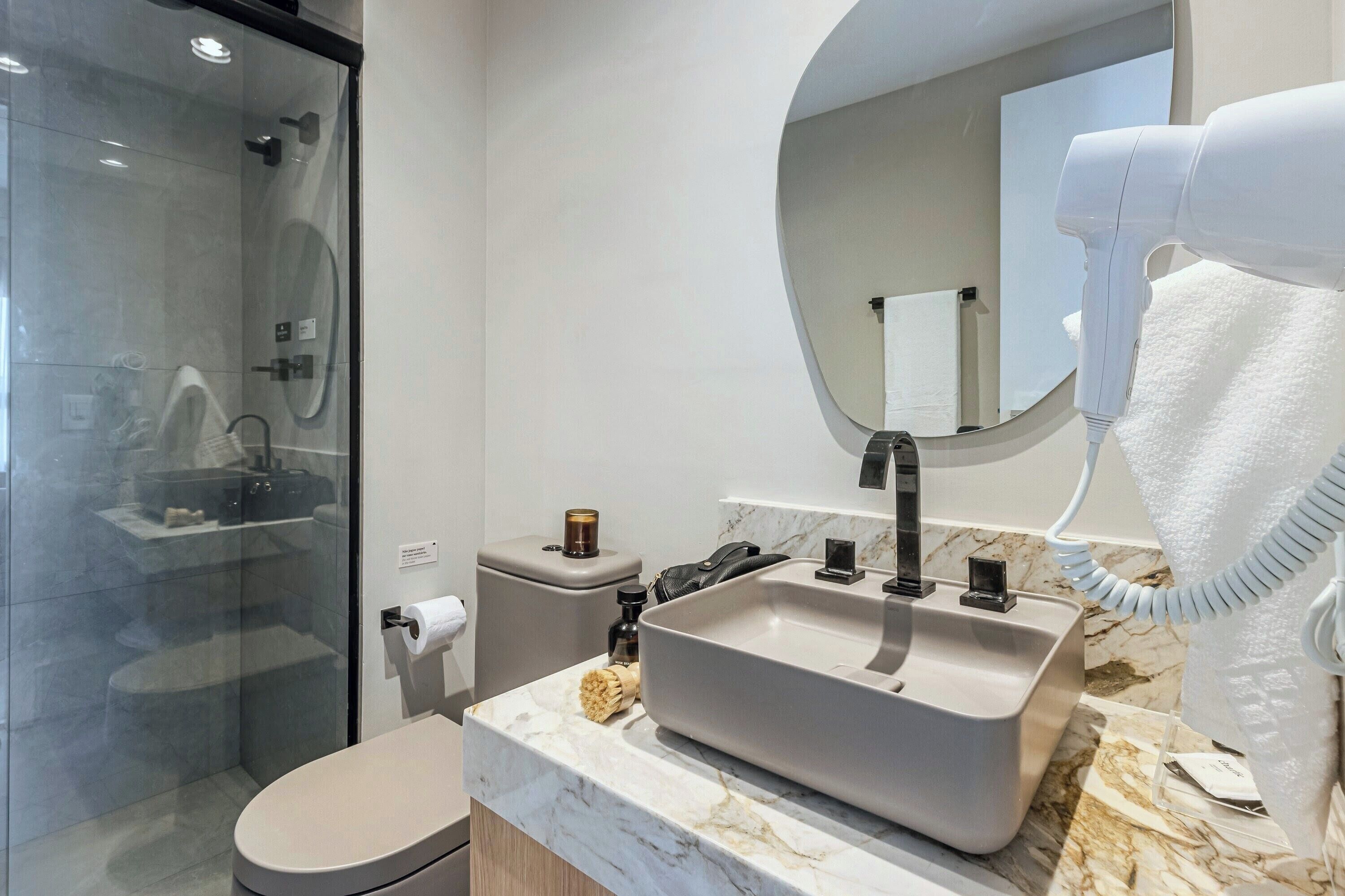 A modern bathroom with a glass shower enclosure, a sink with a marble countertop, and a hairdryer.