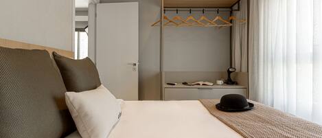 A hotel room with a bed, a wardrobe, a bedside table, and a window with curtains.
