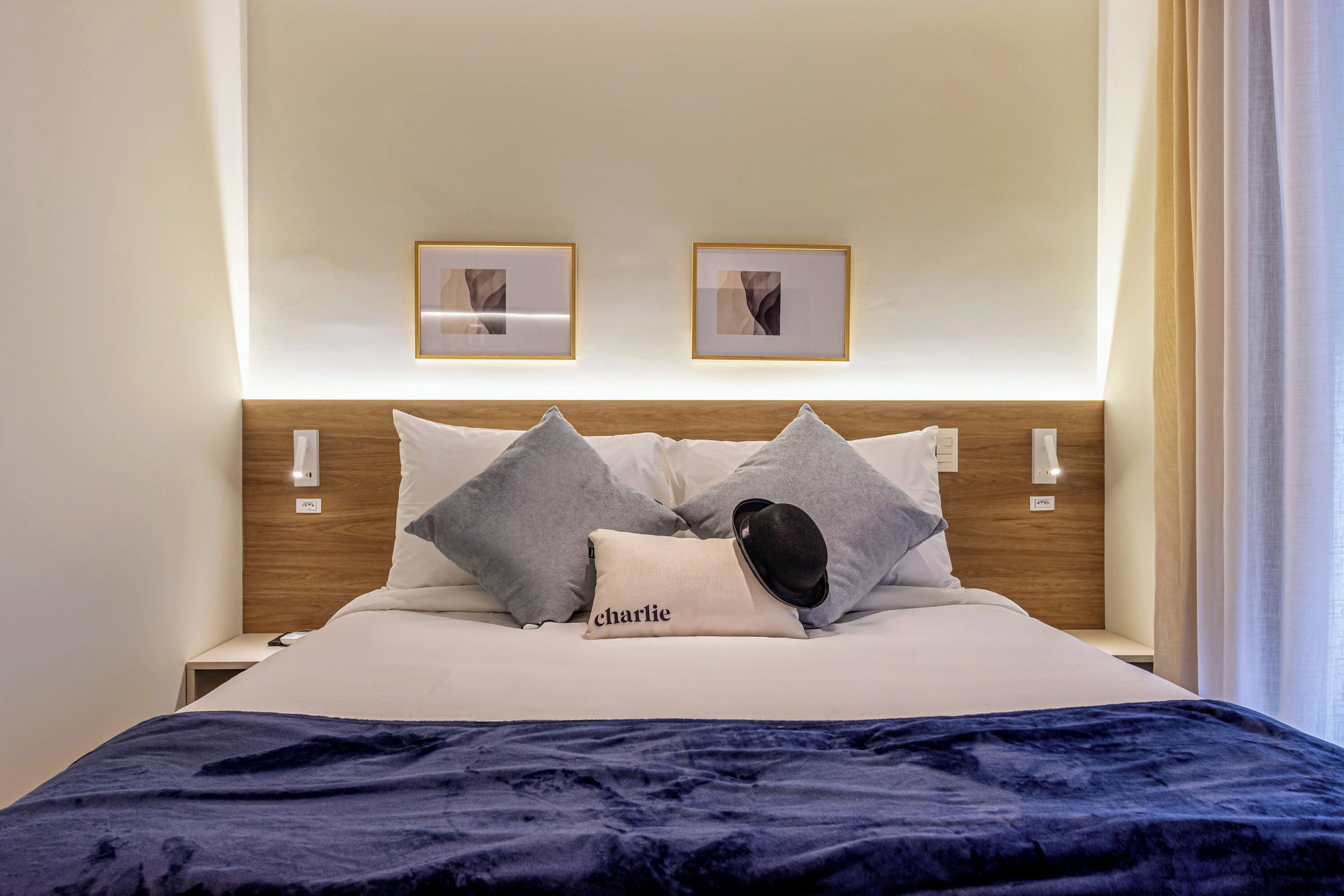Un lit bien fait, recouvert d’une couverture bleu foncé, avec deux oreillers et un coussin portant le nom « Charlie ».